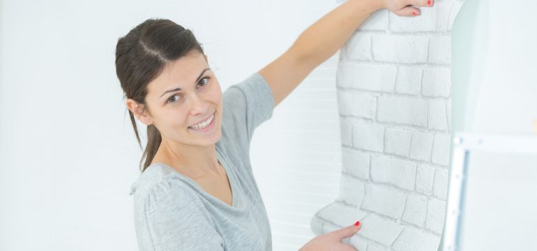 Woman applying wallpaper on wall her apartment. Shows how you can decorate your rental.