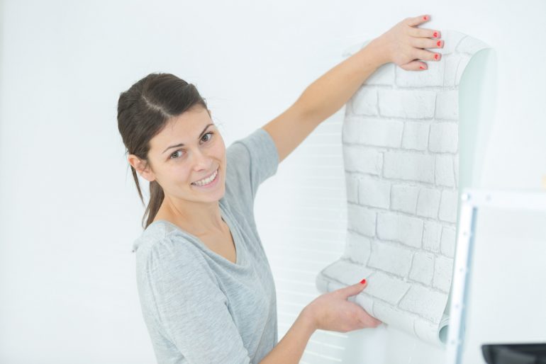 Woman applying wallpaper on wall her apartment. Shows how you can decorate your rental.