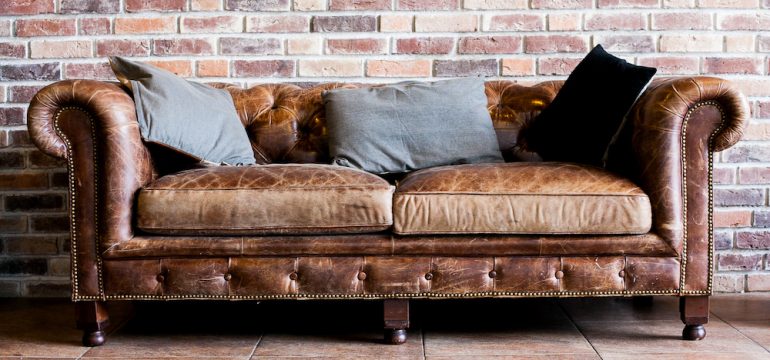 Vintage style of interior decoration with a leather sofa that needs cleaning in against a brick wall in a room.