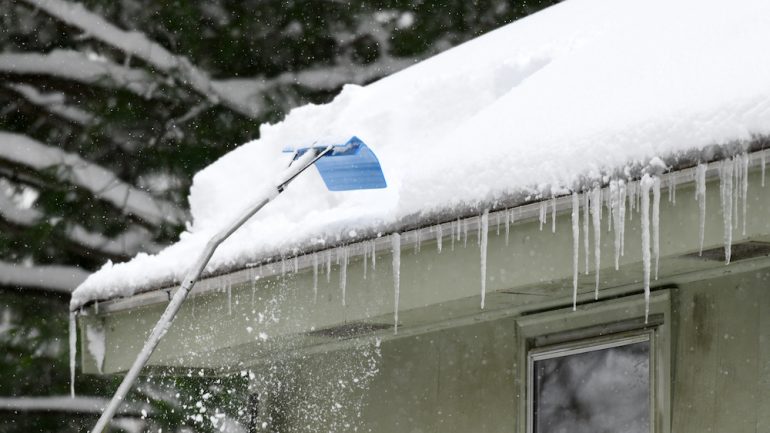 Removing snow off a house roof after a snowstorm.