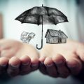 Open hands with an umbrella over a house and auto depicting coverage from an umbrella insurance policy.