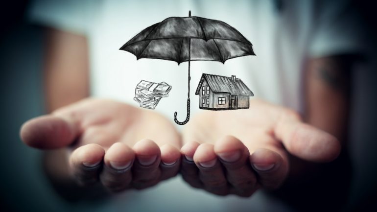 Open hands with an umbrella over a house and auto depicting coverage from an umbrella insurance policy.