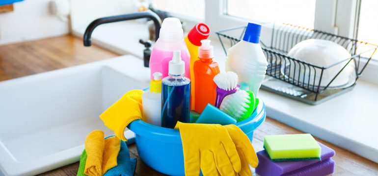 Basket with cleaning items on blurry background white kitchen. Concept of essential items for a new home.