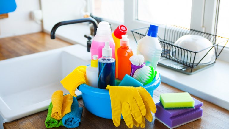 Basket with cleaning items on blurry background white kitchen. Concept of essential items for a new home.