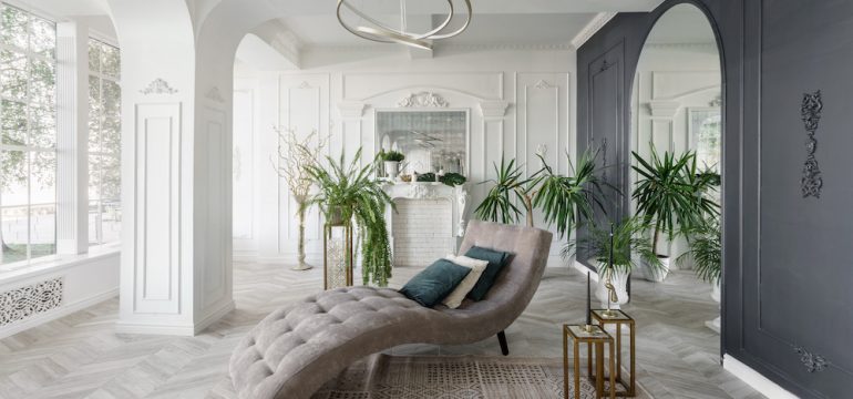 Bright and clean interior design of a luxury living room with parquet wood floors, fireplace, sofa and flowers. Stucco is applied to the load-bearing walls creating a decorative look.
