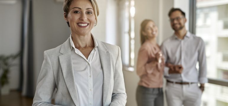 Photo of discount broker real estate agent looking at the camera while her clients are standing in the background.