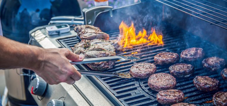 Marinated lamb and beef burgers cooking on an outdoor barbecue demonstrating grilling safety.