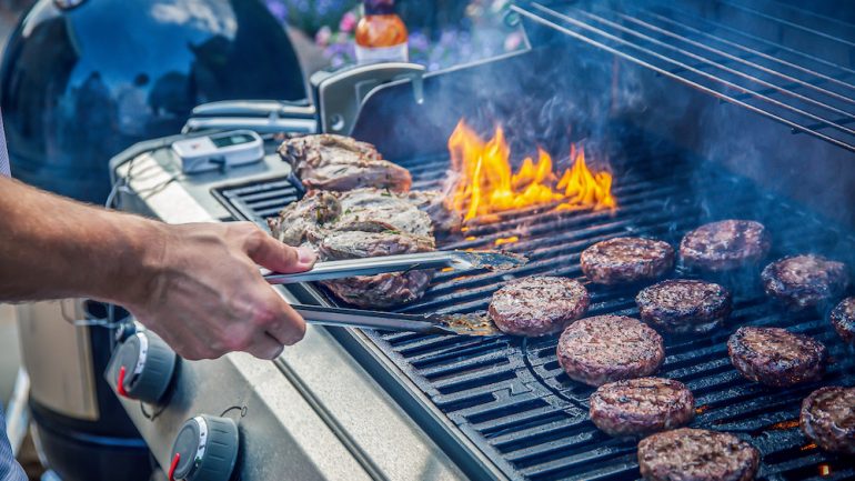 Marinated lamb and beef burgers cooking on an outdoor barbecue demonstrating grilling safety.