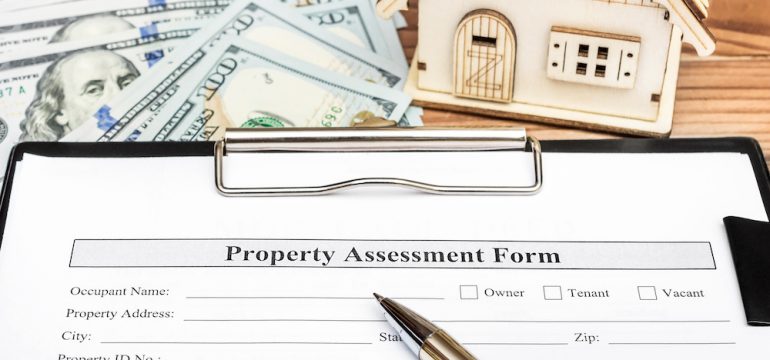 Property assessment form during active option period on clipboard over table with model of house and money.
