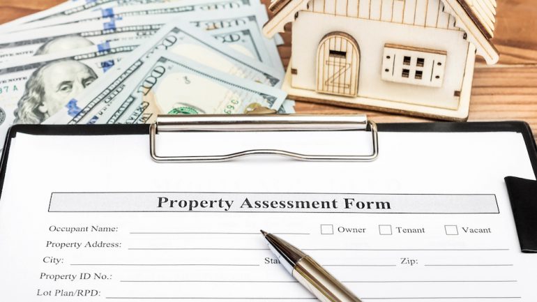 Property assessment form during active option period on clipboard over table with model of house and money.