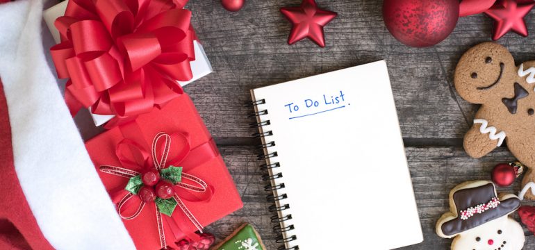 December To-Do list in notebook with christmas gift boxes and red ornament decoration with ribbon bow with snowman cookie and gingerbread man on wooden table top view. Winter holiday planning concept.