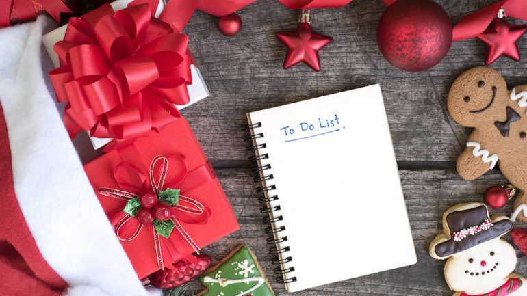 December To-Do list in notebook with christmas gift boxes and red ornament decoration with ribbon bow with snowman cookie and gingerbread man on wooden table top view. Winter holiday planning concept.