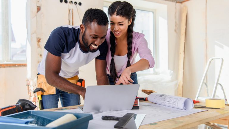 Young african american woman pointing at laptop screen to boyfriend during renovation of home. Wondering about renovating or buying a new home.