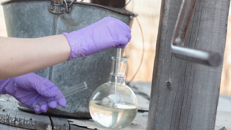 Testing private well water pollution concept. Scientist is taking a water sample for the test close up.