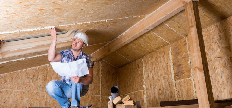 Home inspector wearing a white hard hat while checking a attic ceiling.