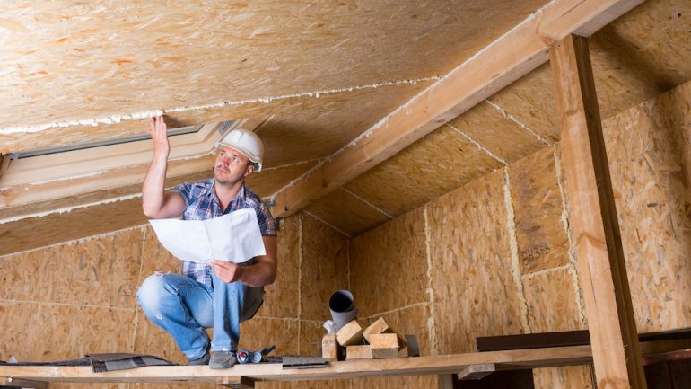 Home inspector wearing a white hard hat while checking a attic ceiling.