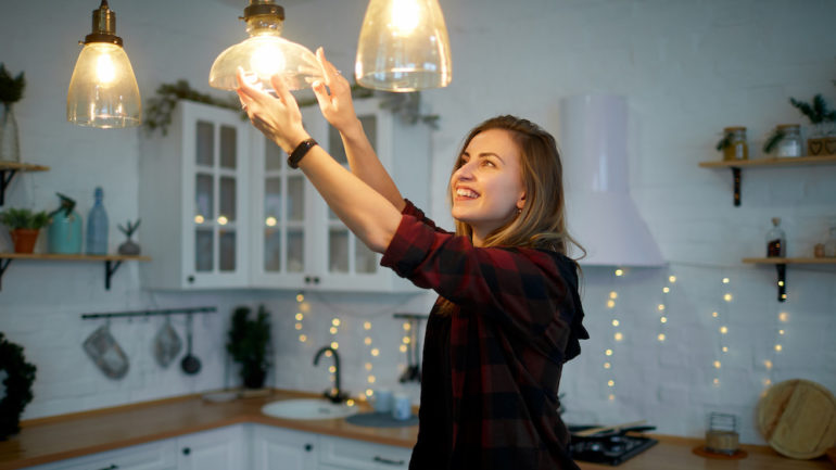 Young happy woman twists a light bulb in the kitchen lamp with the correct light bulb wattage.