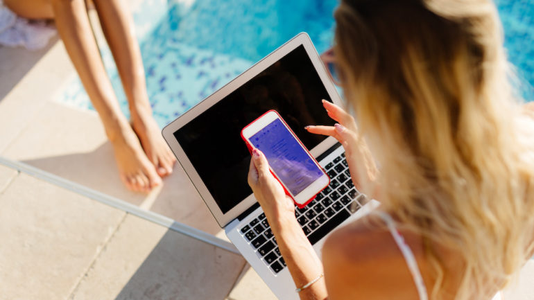 Guest users using laptop and smartphone remotely near swimming pool. multiple devices.