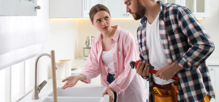 Young woman complaining to the plumber about clogged drains in the kitchen sink.