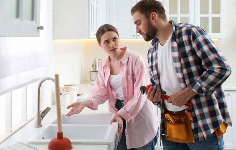 Young woman complaining to the plumber about clogged drains in the kitchen sink.