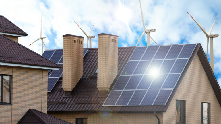 Wind farm near a house with installed solar panels on the roof.