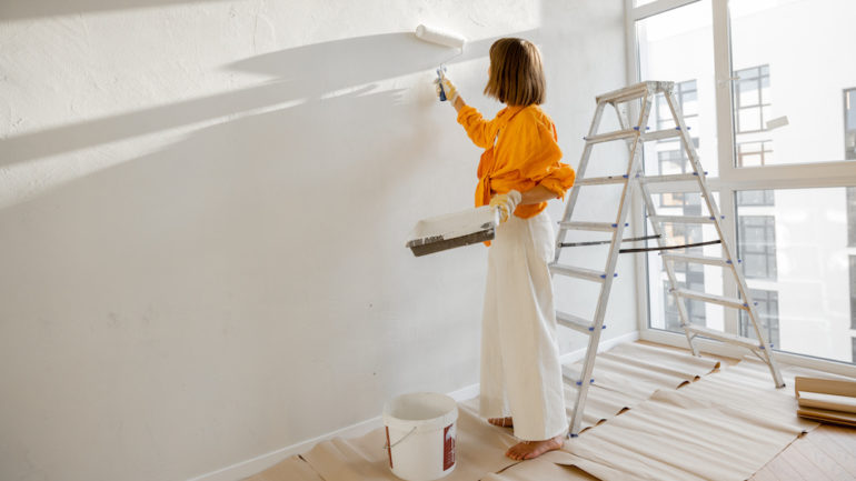 A woman paints the wall in white color to show what to repair before you sell your house.