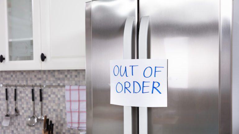 Written text "Out Of Order" message on paper taped on closed refrigerator door In a kitchen. Demonstrates what to do with a broken appliance.