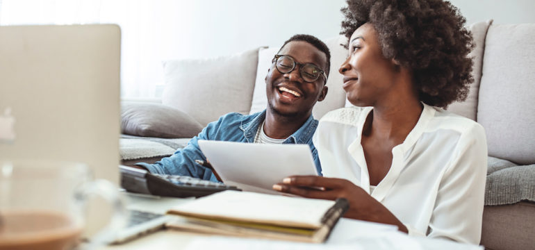 Young married couple doing their paperwork together and analyzing their changing insurance needs on their laptop.