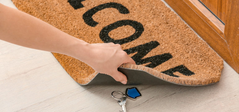 Woman hiding spare keys under house door mat.