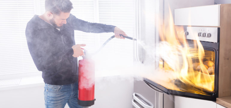 Man using red fire extinguishers to stop a fire in a home kitchen oven.