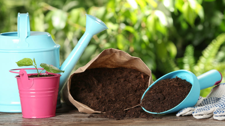 Composition with bag of soil and gardening equipment on wooden table against blurred background.