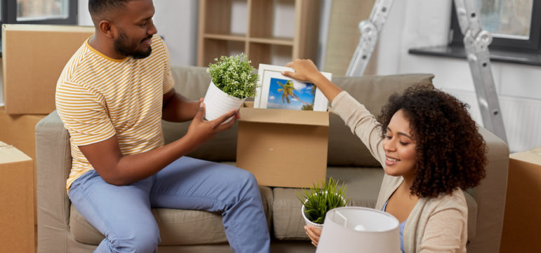 Happy couple combining furnishings in their new home. Unpacking boxes with plants, pictures and lamps.