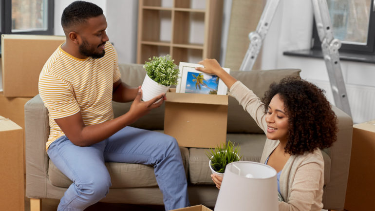 Happy couple combining furnishings in their new home. Unpacking boxes with plants, pictures and lamps.