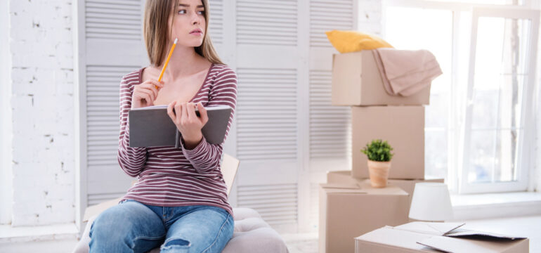 Neat and organized young woman sitting on an ottoman and reviewing a moving checklist.