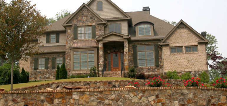 A luxury home built on a hill with a stone exterior and hardscape wall in front.