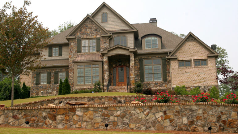 A luxury home built on a hill with a stone exterior and hardscape wall in front.