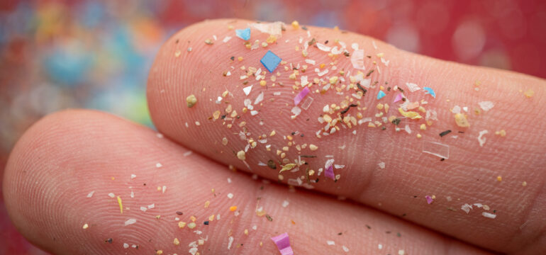 Microplastics particles on a human finger for scale.