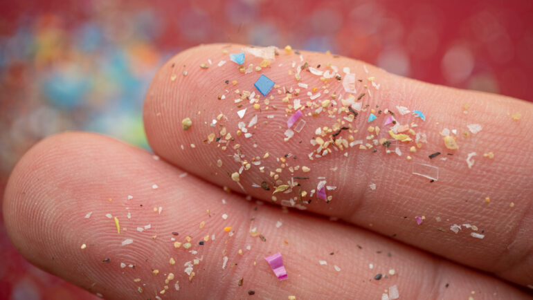 Microplastics particles on a human finger for scale.