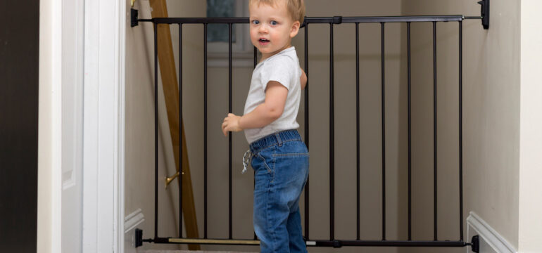 Cute toddler approaching the safety gate of stairs at home.