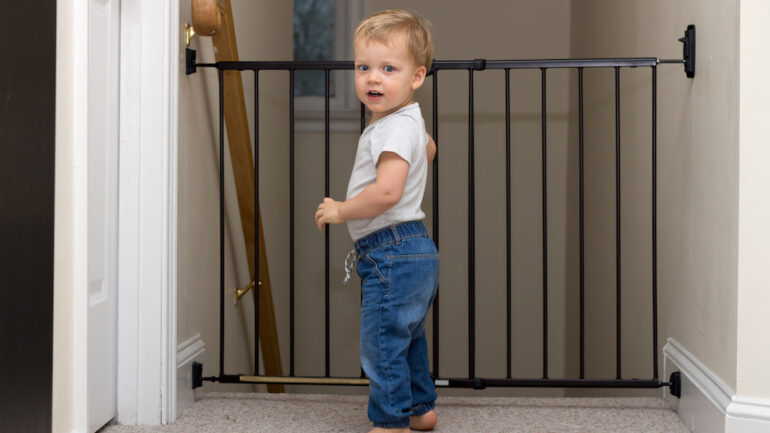 Cute toddler approaching the safety gate of stairs at home.