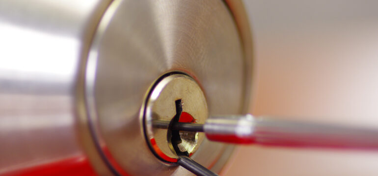 Closeup hands of locksmith using metal pick tools to open a locked door.