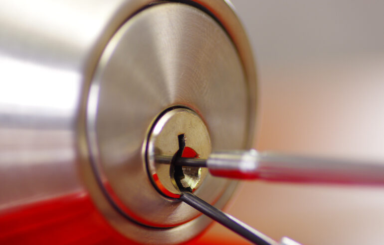 Closeup hands of locksmith using metal pick tools to open a locked door.