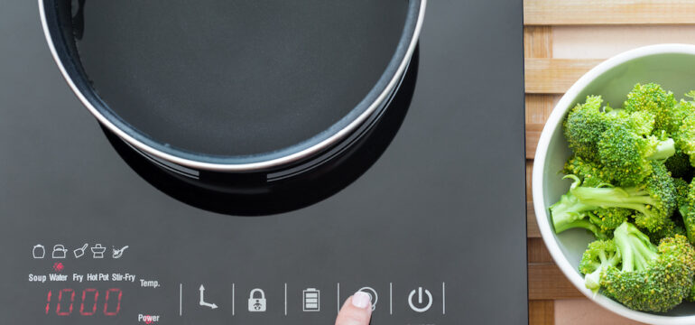 Photo of a woman's hand using induction cooking to make broccoli in a modern kitchen.