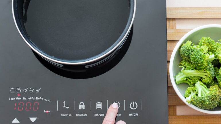 Photo of a woman's hand using induction cooking to make broccoli in a modern kitchen.