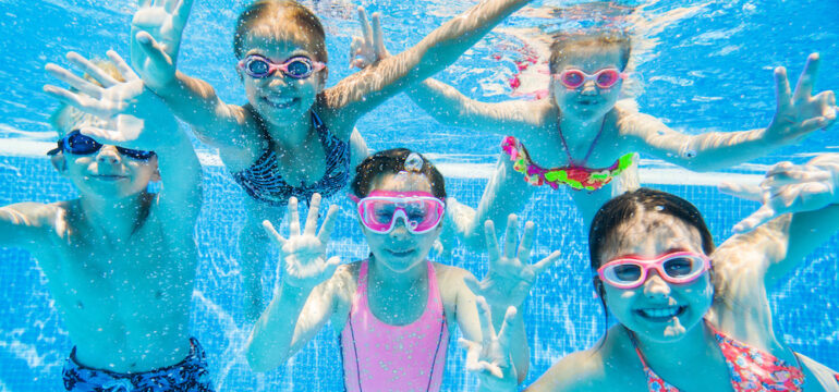 Smiling children swimming underwater in an inground pool demonstrates the benefits of saltwater versus chlorine water.
