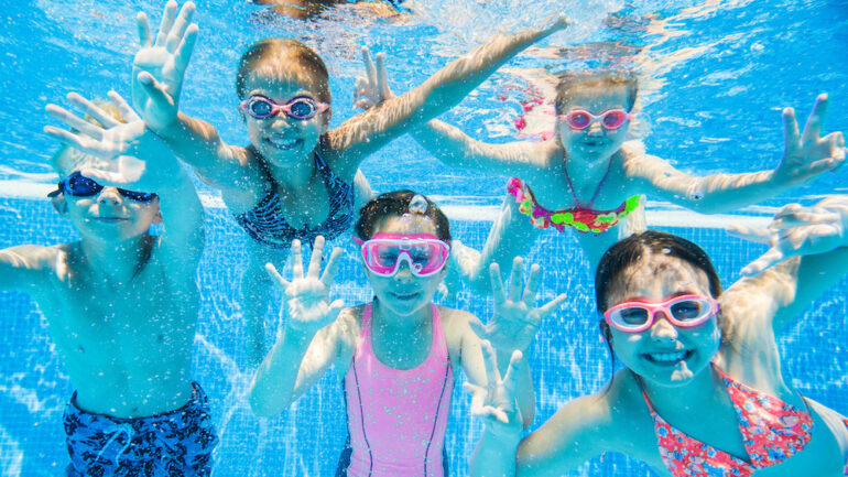 Smiling children swimming underwater in an inground pool demonstrates the benefits of saltwater versus chlorine water.