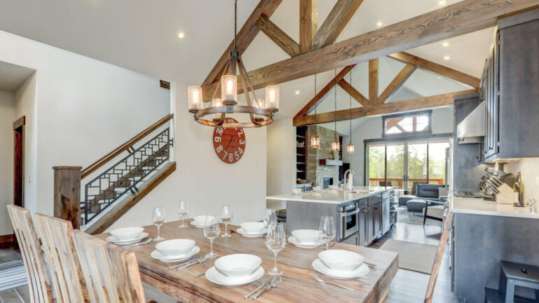 Amazing dining room near modern and rustic luxury kitchen with vaulted ceiling beams, long island with white quartz countertop, and dark wood cabinets.