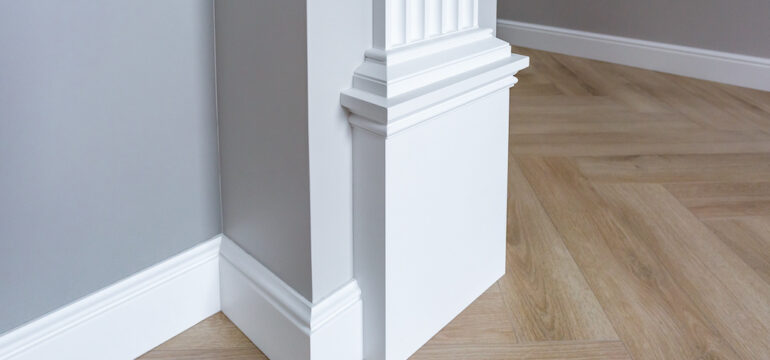 Detail of corner flooring with intricate crown molding with white trim paint against grey walls.