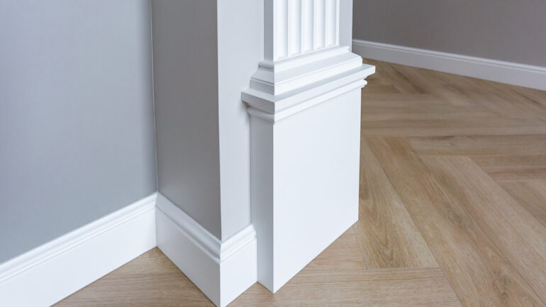 Detail of corner flooring with intricate crown molding with white trim paint against grey walls.