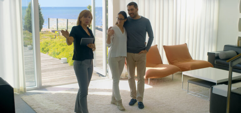 A professional real estate agent shows stylish modern houses to a young couple.